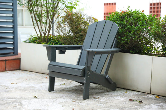 Gray HDPE folding Adirondack chair with wood texture and dual cup holders, designed for outdoor coastal settings.