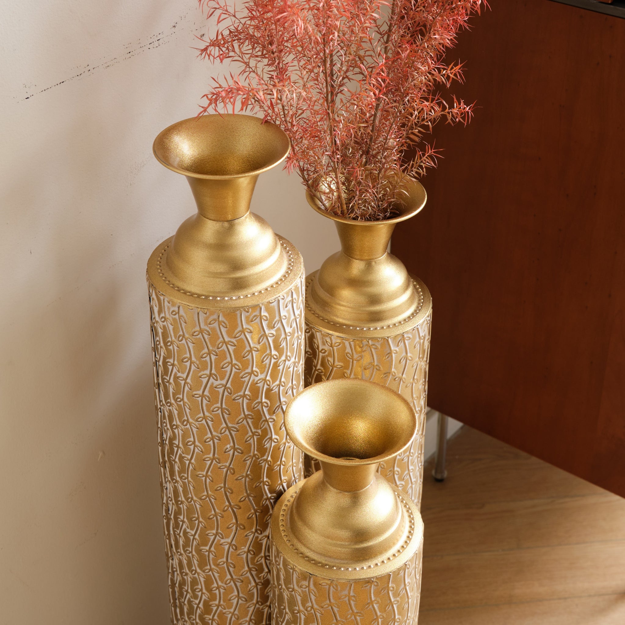 Set of three Anthony & Home Heritage Collection gold distressed metal vases with vine patterns for living room decor.